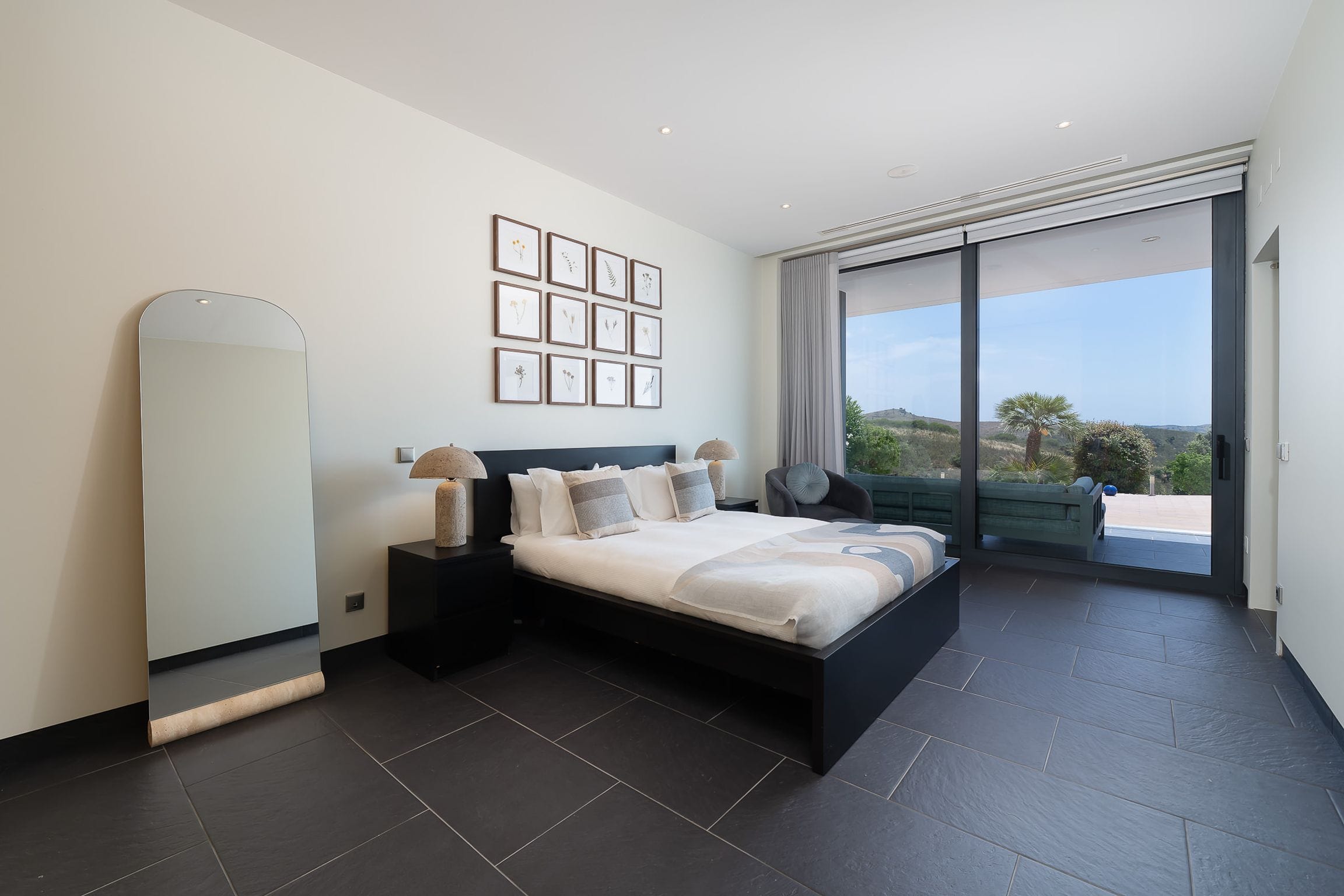 Calm double bedroom with botanical prints, stone lamps and sliding glass doors to the terrace