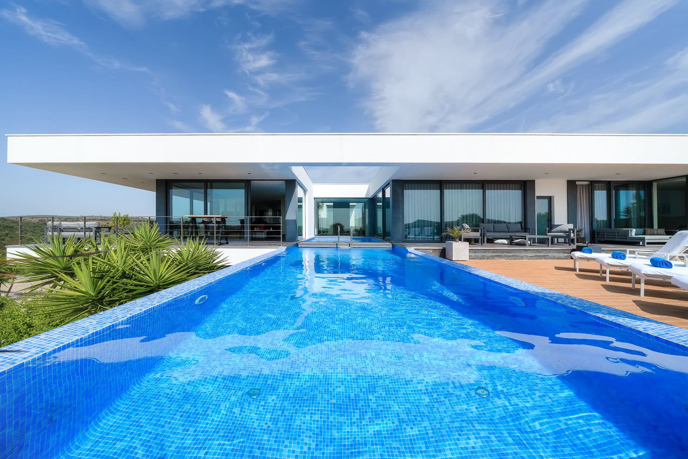 Long infinity pool leading the eye towards the glass-fronted villa beneath a wide flat roof